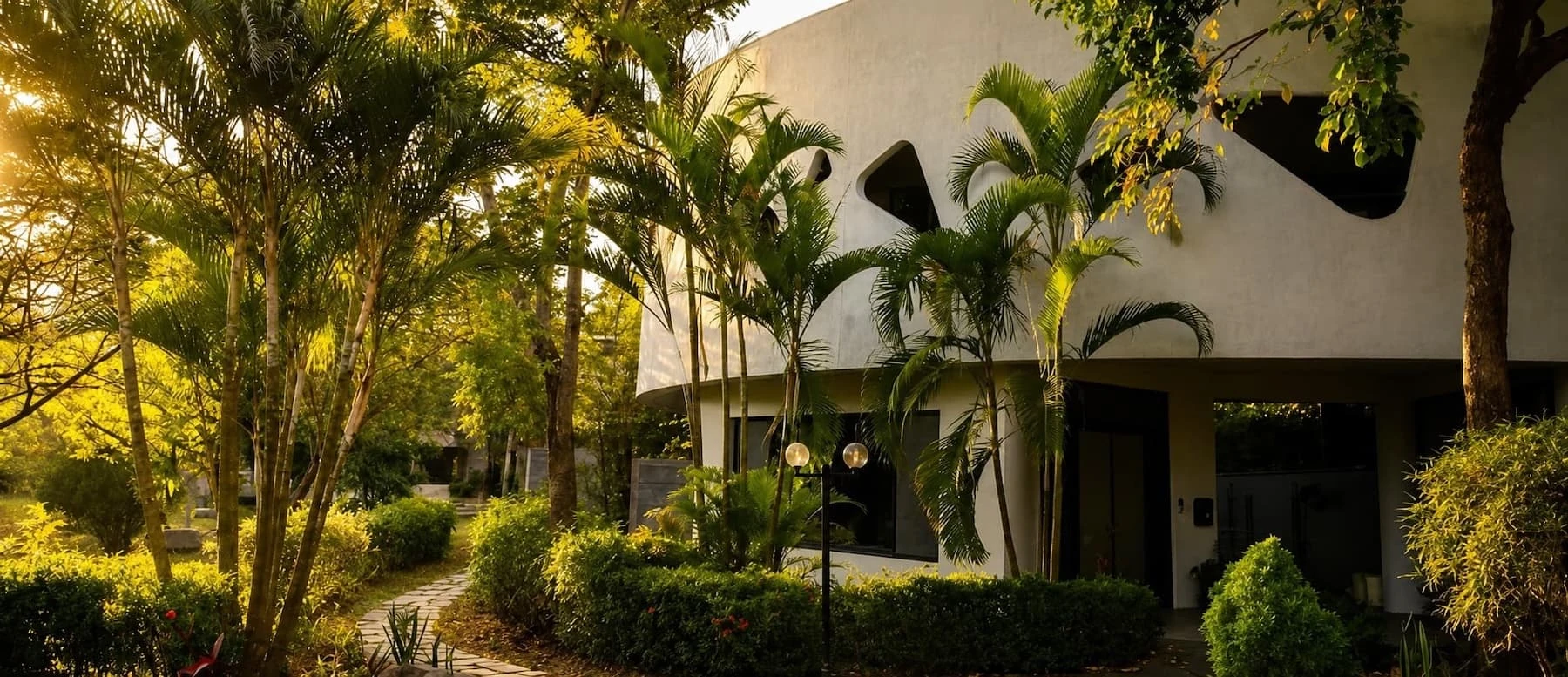 A white meditation center shaded by palms in warm afternoon light