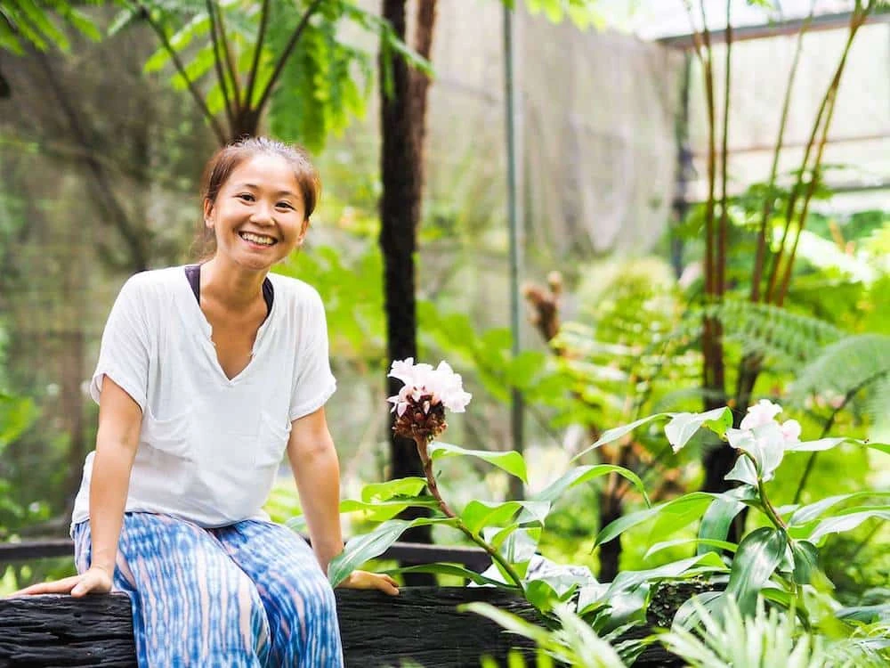 A smiling gardener seated among vegetables in a greenhouse